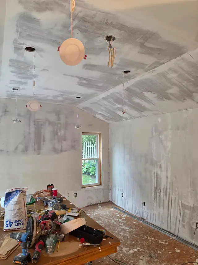 A ceiling and walls patched in white compound, a work table of tools in the middle of the room.