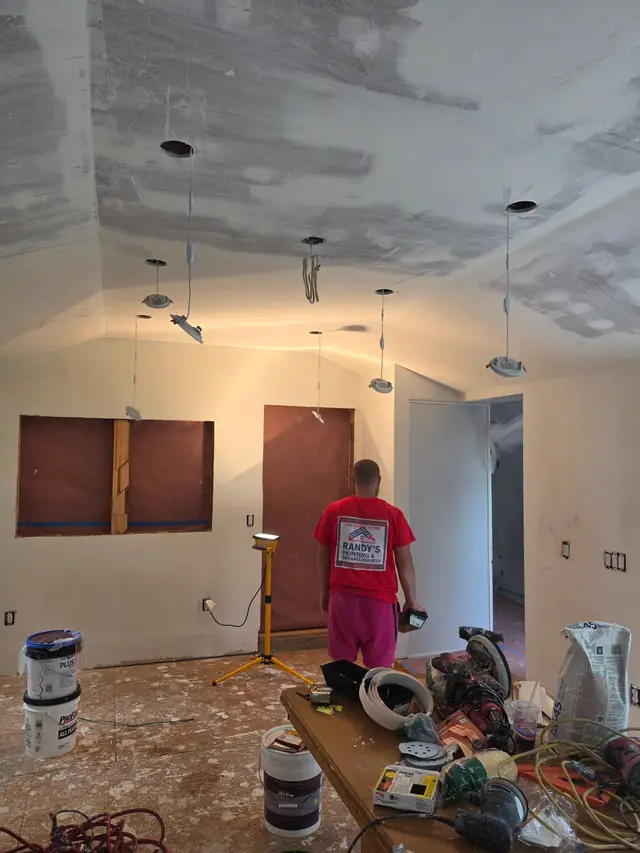 A room with its ceiling part-way through a skim coat, a painter working beneath it among tools and buckets.