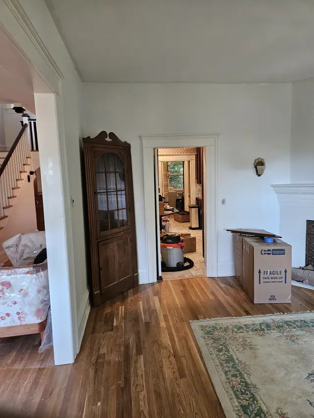 A period dining room with white walls, a dark wood corner cabinet, and a doorway looking through to the staircase.