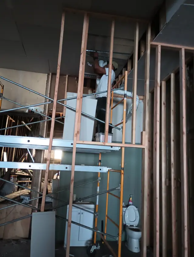 Bare stud framing and a scaffold in a room being rebuilt, before any drywall goes up.
