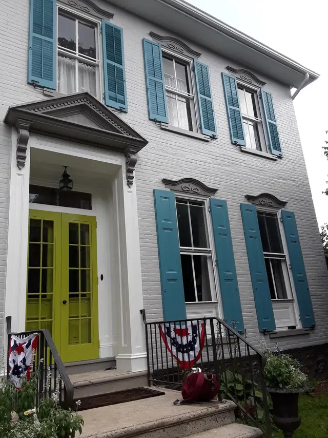 A Federal-style house of painted white brick with teal shutters and chartreuse double doors beneath a pediment.