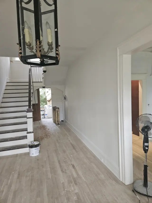 The same period foyer finished: white walls, a white staircase and a hanging lantern over a pale floor.