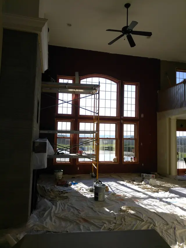 A tall great room with arched windows, a scaffold set up and the floor covered in drop cloths.