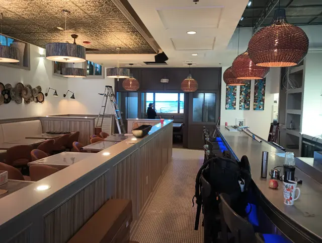 A restaurant interior with a long bar, booth seating and woven pendant lights.