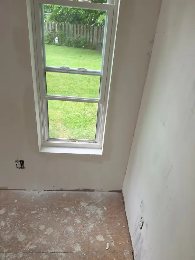 Smooth white walls beside a tall window, the floor still covered with paper.