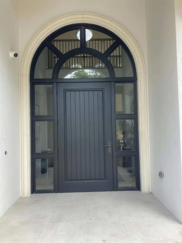 An arched black steel entry door with sidelights and a fanlight, set in a cast-stone surround in a white stucco wall.