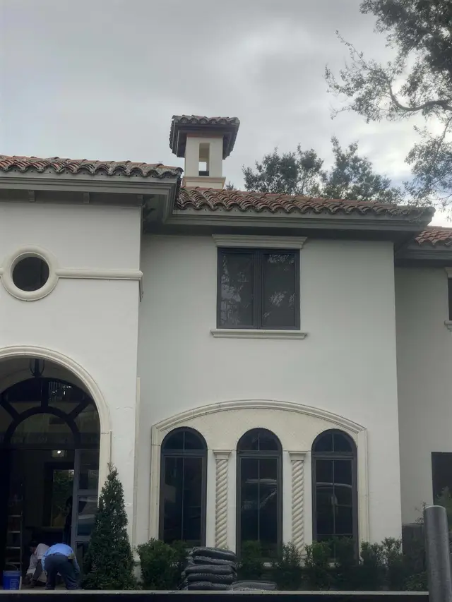 A white stucco Mediterranean-style house with a terracotta roof, a round window and arched windows with cast-stone trim.